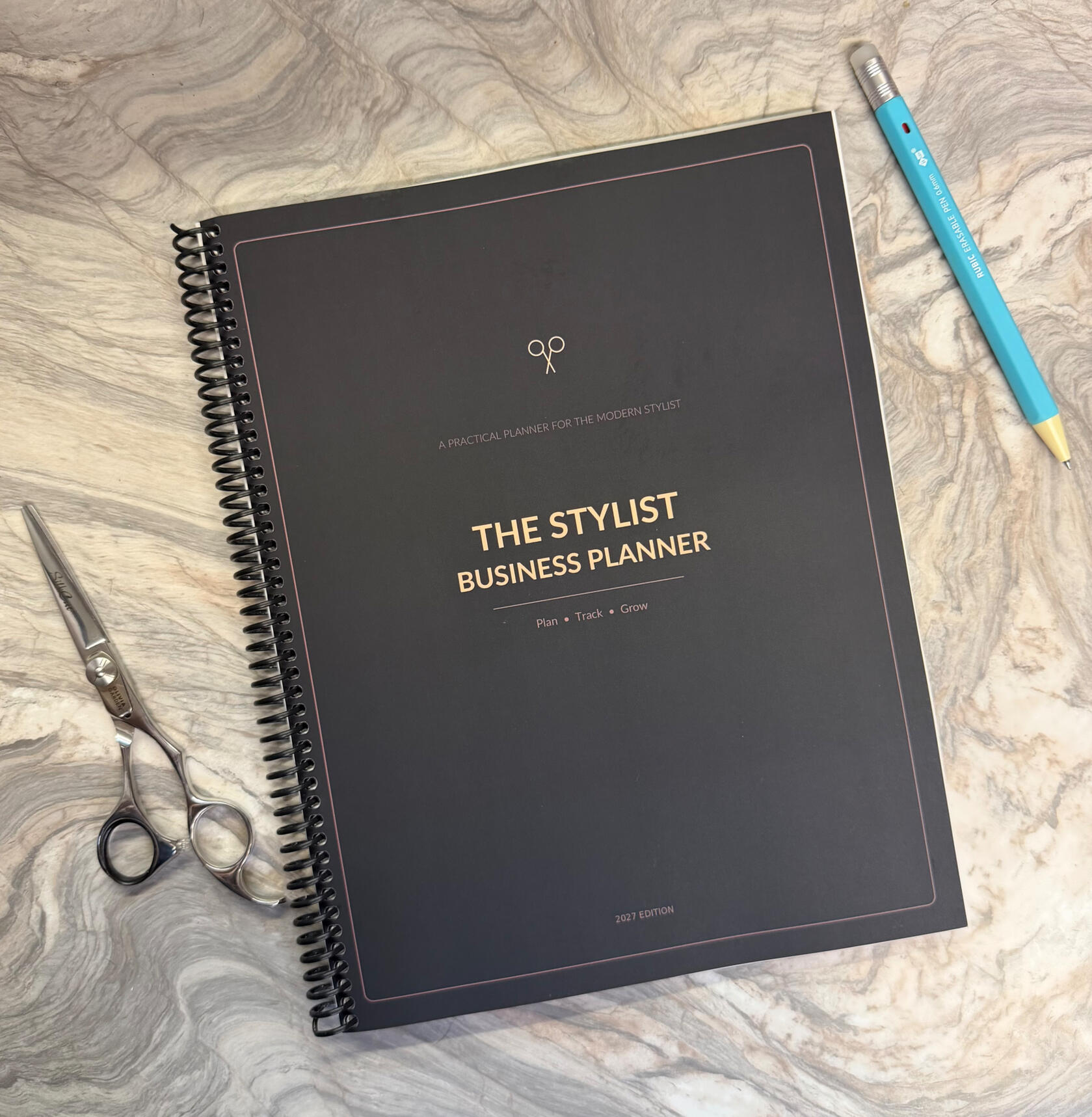 Spiral-bound business planner for hairstylists, shown on a real salon station